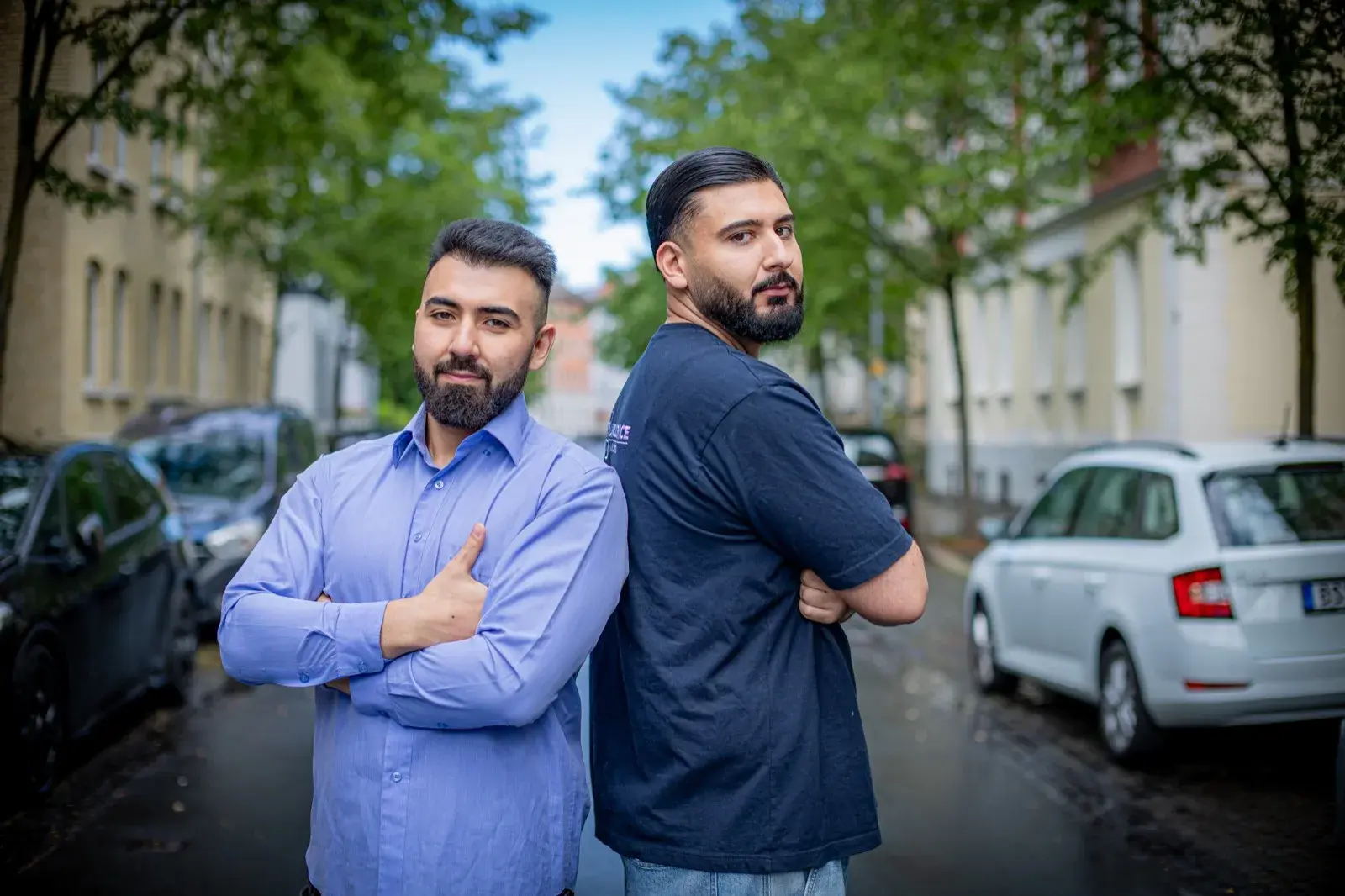 Umut und Can, die beiden Gesellschafter, stehen Rücken an Rücken mit verschränkten Armen auf einer Wohnstraße in Braunschweig